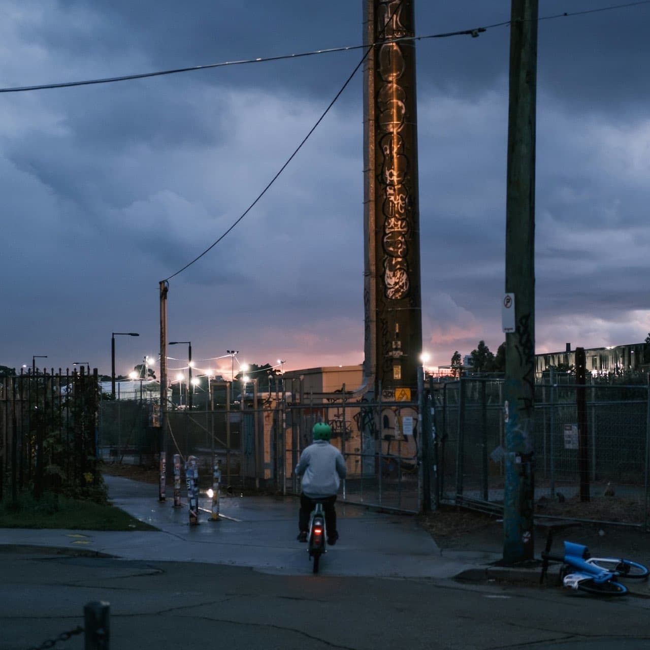 An e-bike rider in a green helmet heads onto a shared path at dusk, rear light on